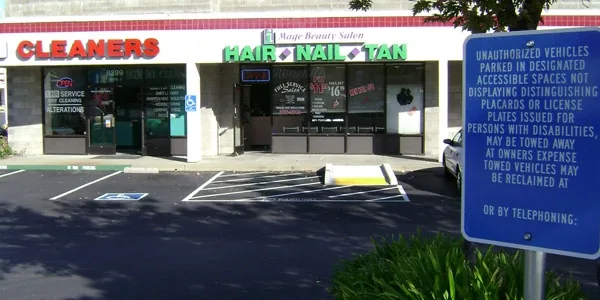 Strip-center lot with a new accessible stall and tow-away sign in front of a cleaners