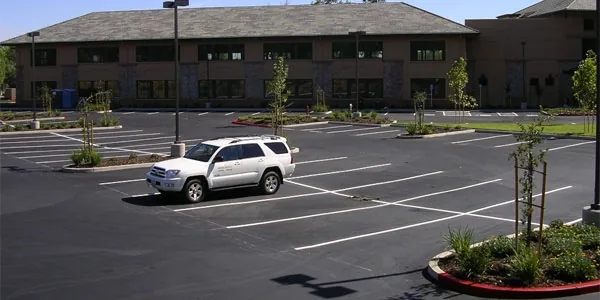 Office building lot, newly paved and striped, with planters and a white SUV