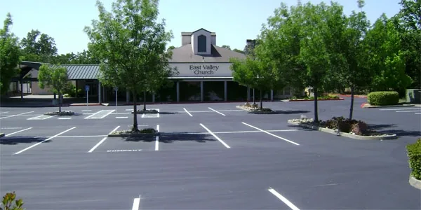 Striped parking lot in front of a building with a cupola, trees and planters along the edge